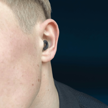 Close-up of a person wearing a black hello calm ADHD ear plug against a dark background